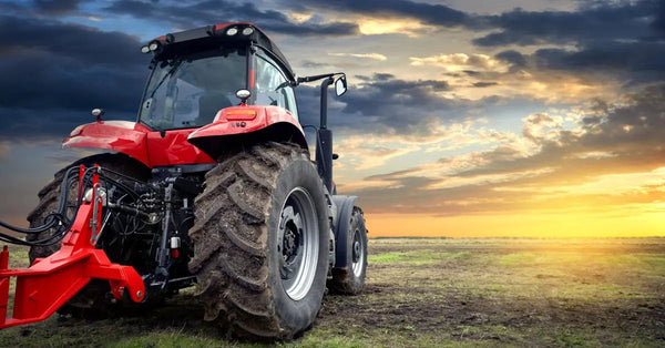 A red tractor with a rear-mounted attachment is parked in an open field under a dark and cloudy sky.