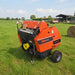 TRB50N round hay baler standing in a green field with farm buildings behind it